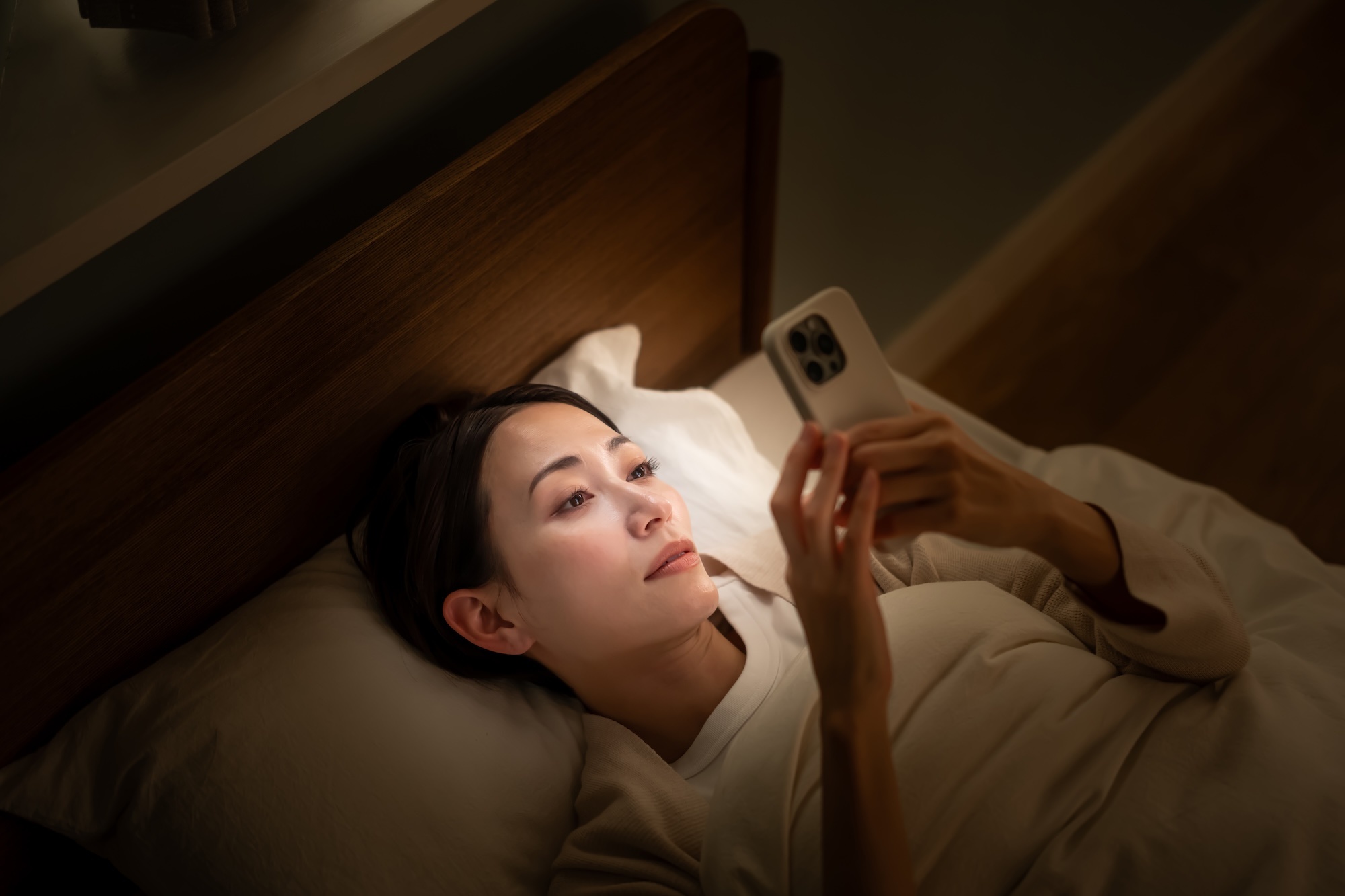 ベッドに入ってスマホを使う女性