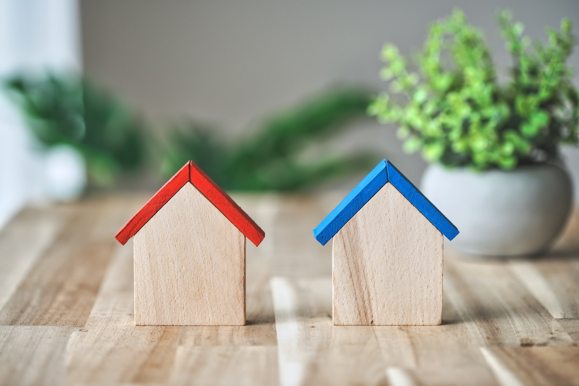 木目のテーブルに置かれた2つの家と観葉植物
